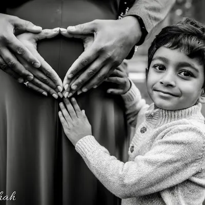 A beautiful black and white portrait showing the hands of the parents and older brother forming a heart on the baby bump. This is a powerful symbol of a family's love and anticipation.