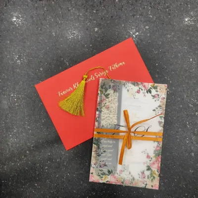 A complete view of a vibrant and elegant invitation suite. It includes a floral vellum wrap tied with a ribbon, a main invitation card, and a bold red envelope with the couple's names in gold foil.