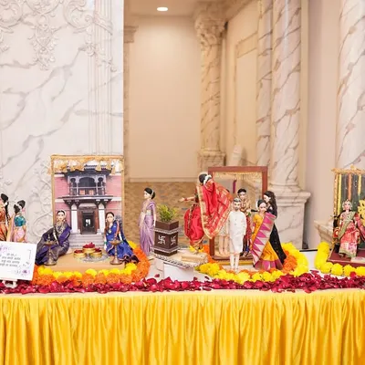 A wide view of a complete *dohale jevan rukhwat* setup. The display includes multiple handcrafted doll scenes, from a Ganesha pooja to family gatherings, all tied together with vibrant marigold and rose petal decorations.