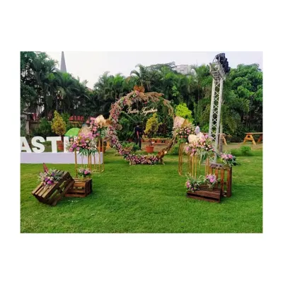 An open-ground wedding setup featuring a rustic-chic theme. The centerpiece is a large circular backdrop with the words 'Better Together', surrounded by floral arrangements on wooden crates and stands.