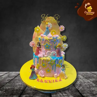 A dreamy two-tier cake featuring several Disney princesses. The pastel colors, star decorations, and drip effect create a magical backdrop for figures of Cinderella, Ariel, and others.