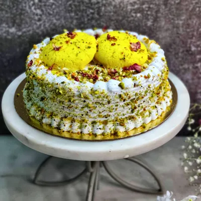 My signature Rasmalai Cake, presented on a marble stand. I build this dessert with a soft, saffron-infused sponge, layer it with creamy rabdi, and top it with two large, luscious rasgullas for a truly impressive centerpiece.
