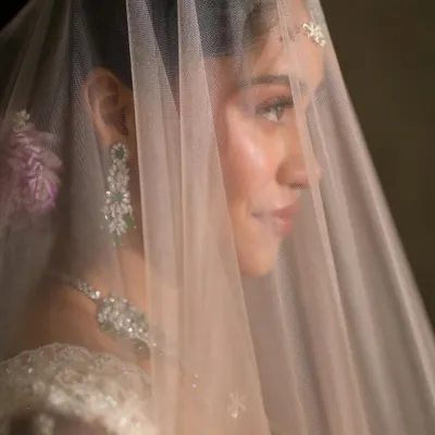 An ethereal bridal look behind a delicate veil. Dressed in a dreamy white and pink lehenga with emerald diamond jewels, the makeup is subtle, clean, and natural to enhance her glow.