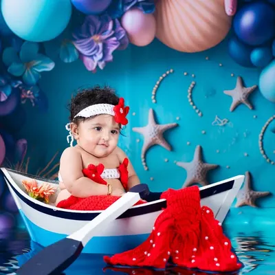 Our little mermaid is ready for an ocean adventure! This vibrant, underwater-themed setup features a custom boat, a knitted mermaid tail, and a sea of colorful balloons and starfish.
