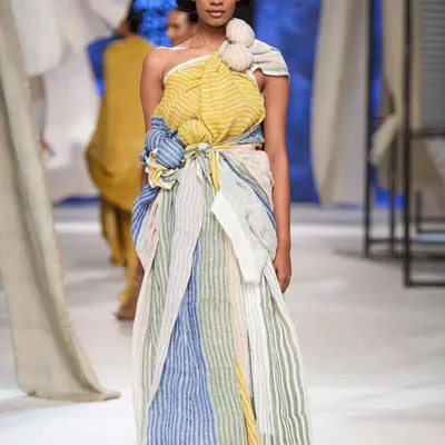 A stunning runway look for designer Anavila Misra at Lakmé Fashion Week. The makeup is clean and earthy, paired with a structured bun to complement the handwoven, sustainable fabric and intricate draping of the garment.