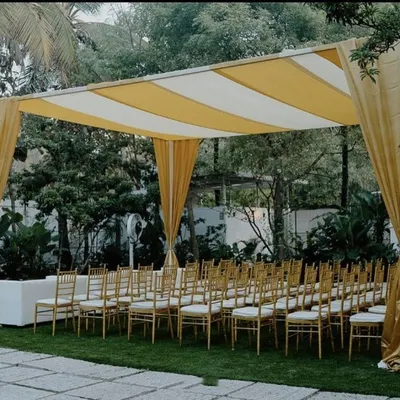 This image shows the guest seating area for a Haldi ceremony. The space is defined by a large canopy with yellow and white striped fabric and matching yellow drapes, creating a bright and cheerful environment.