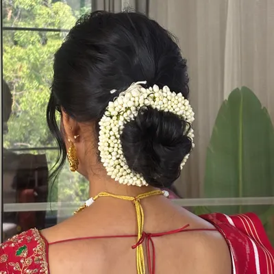 A closer look at this flawless traditional bridal bun. The hair is smoothly swept back and secured into a perfect low bun, encircled by a thick, fresh jasmine gajra. This is a classic South Indian bridal hairstyle that is always in vogue.