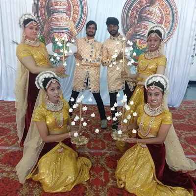 To provide a traditional and warm welcome for your guests, I can arrange for performers in cultural attire. This group is positioned at the entrance for a wedding ceremony, holding decorative candle stands.