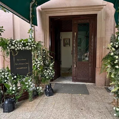 We create elegant welcome areas that set a sophisticated tone. This setup features a classic black and gold sign surrounded by lush arrangements of white roses and greenery.