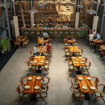An overhead view of the main dining hall at Pincode 24. This perspective shows the flexible seating arrangement with a mix of low and high tables, the expansive concrete-texture tile flooring, and the impressive scale of the double-height space leading to the bar.