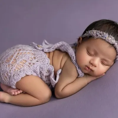 A classic side lying pose on a soft lavender backdrop. The baby is dressed in a delicate lace romper and a matching headband, creating a sweet and serene portrait.