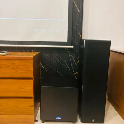 A complete home theater system ready for action, featuring floor-standing speakers, a powerful subwoofer, and a large projector screen. This is how you get movie nights that feel just like the cinema.