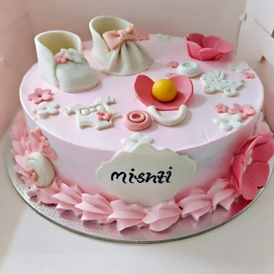 A sweet welcome cake for a baby girl, decorated with edible baby shoes, a pacifier, and other cute baby items.