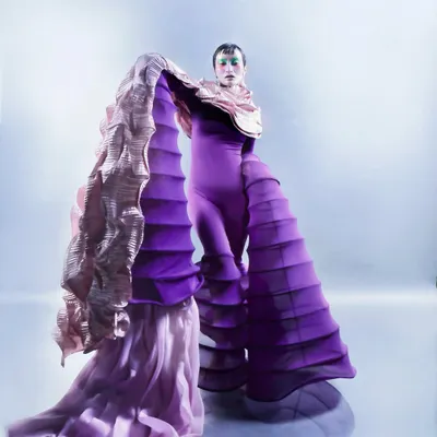 A full-length view of the avant-garde styling in 'Chemical Reaction,' showing the interaction between the structured purple garment and the flowing pink fabric. The composition emphasizes the grand, sculptural nature of the outfit.