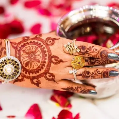 It's all in the details. This shot focuses on the bride's hand, showcasing the intricate mehendi design, the beautiful rings, and the traditional bracelet. The scattered rose petals add color and context to the image.