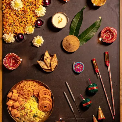 A festive flatlay showcasing the essentials of a Maharashtrian Diwali. This frame includes 'faral' like chakli and shankarpali, diyas, flowers, and firecrackers, artistically arranged to capture the complete essence of the celebration.