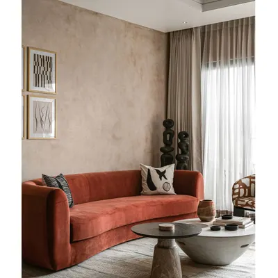 The living room in Project ASA is defined by its textural lime-washed walls and a show-stopping rust-orange curved sofa. This space is all about creating a warm, inviting atmosphere with bold color and organic forms.