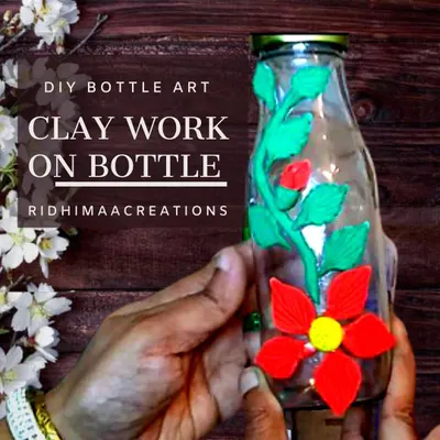Don't throw away old glass bottles. This image shows how you can upcycle a simple bottle by decorating it with floral designs using air-dry clay, turning it into a beautiful decor piece.