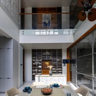 A grand dining area in a duplex home, featuring a double-height ceiling and a glass-paneled mezzanine. The custom crockery unit and island counter add both functionality and a touch of luxury.