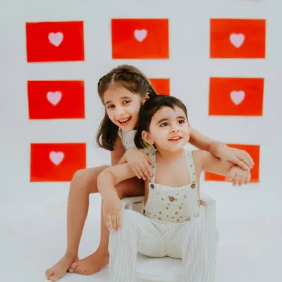 A sweet moment between two sisters during their studio photoshoot. The simple backdrop of red hearts makes their connection the main focus.