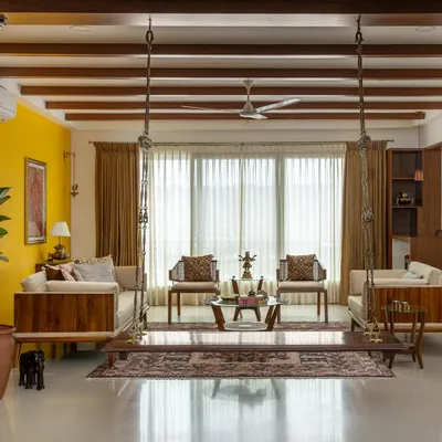 The 'Vasudhalayah' living room is a tribute to Indian heritage. We used antique Chettinad pillars, a traditional swing, and a bold yellow accent wall to create a space that is earthy, vibrant, and full of character.