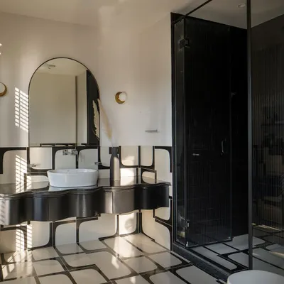 A bold monochrome bathroom with custom-designed tile patterns and an undulating black vanity. The sculpted countertop adds an artistic touch, while soft curves balance the geometry.