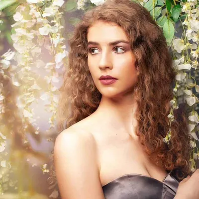 A dreamy beauty portrait with a soft, ethereal feel. The model is surrounded by delicate white flowers, and the lighting is diffused to create a gentle glow on her skin and highlight her natural features.
