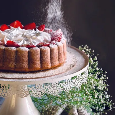 A stunning shot of a strawberry-topped cake being dusted with powdered sugar, capturing a moment of kitchen magic.