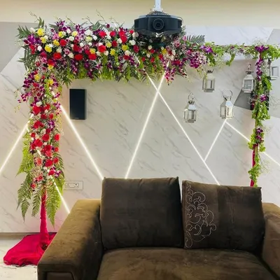 An L-shaped floral arch designed to fit perfectly in a living room for a small function. This arrangement uses a mix of colorful flowers and ferns to create a beautiful frame over the main seating area without taking up too much space.