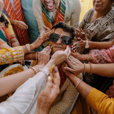 The perfect candid Haldi moment. The groom is surrounded by family, all joyfully applying turmeric paste. It's chaotic, fun, and full of love.