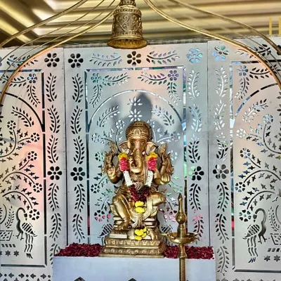 A divine beginning with a beautiful Ganpati idol set against an intricate white jali backdrop, adorned with temple bells, symbolizing blessings and auspiciousness.