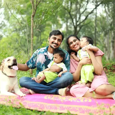 A beautiful family portrait in an orchard, featuring a happy couple with their twin babies and their first child, Snowy the Labrador, by their side.