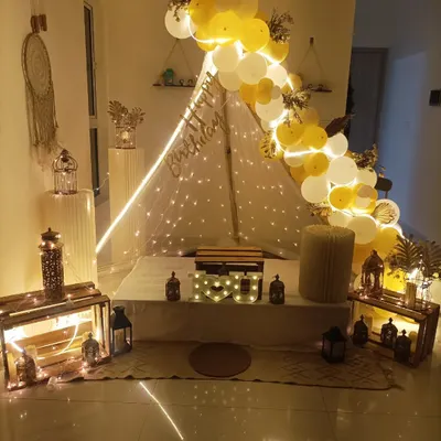 A beautiful and bright birthday cabana setup in white and yellow. The tent is surrounded by decorative lanterns, wooden crates, and a lovely balloon arch.