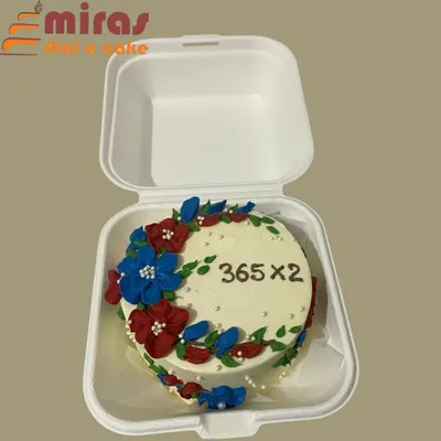 Celebrating a second anniversary, this bento cake features a wreath of delicate, hand-piped flowers in red and blue. It's a simple yet elegant way to mark a special occasion like "365 x 2" days together.