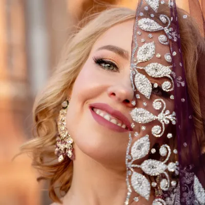 A joyful close-up portrait of a model in a traditional Indian lehenga. She peeks from behind an intricately embroidered dupatta, with a genuine smile that lights up the frame.