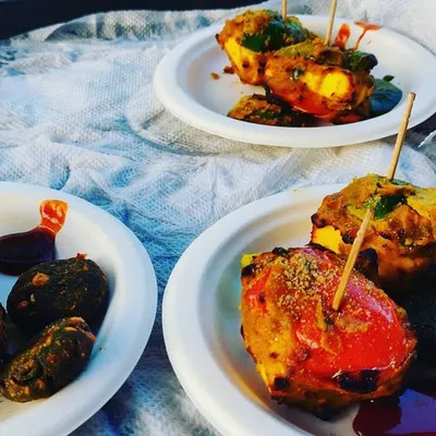 A plate of assorted tandoori appetizers, including paneer tikka and hara bhara kabab, served with mint chutney. A perfect starter for any event.