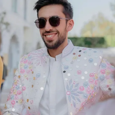 A closer look at the groom's jacket from our coordinated family ensemble. The white base is brought to life with multi-colored floral embroidery and mirror work, perfectly matching the bride's outfit for a cohesive and stylish look.