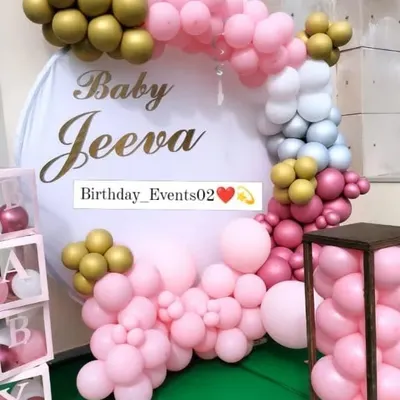 Our classic baby shower backdrop is perfect for photos. This setup features a circular frame decorated with pink, white, and gold balloons, personalized with the name 'Baby Jeeva' in a beautiful script.