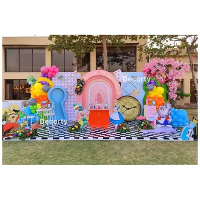 A sprawling, vibrant "Alice in Wonderland" setup in a garden. This whimsical scene features multiple photo ops, including a keyhole cutout, a Mad Hatter tea party, and character props.
