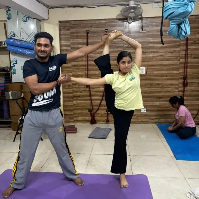 An instructor provides support in a standing split variation, helping the student achieve greater height and maintain balance. This hands-on technique ensures stability in advanced balancing poses.