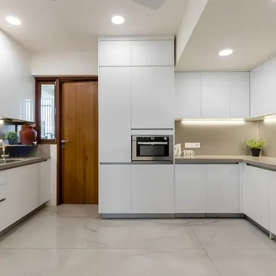 This all-white U-shaped kitchen is a study in modern minimalism. The handleless cabinets, integrated microwave, and under-cabinet lighting create a seamless and brightly lit workspace.