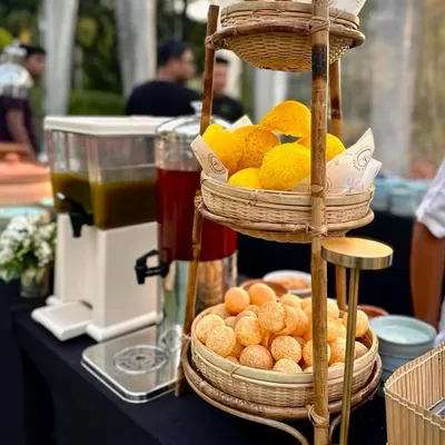 A beautiful bamboo stand presents the elements for a classic pani puri station. It holds crispy puris and large glass dispensers for sweet and spicy flavored waters, ready for guests to create their own chaat.