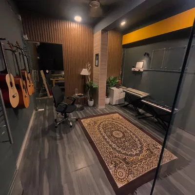 A wide view of our main studio room at HSR Layout. It showcases the blend of warm wood paneling, comfortable seating, and professional equipment like the keyboard and wall-mounted guitars.