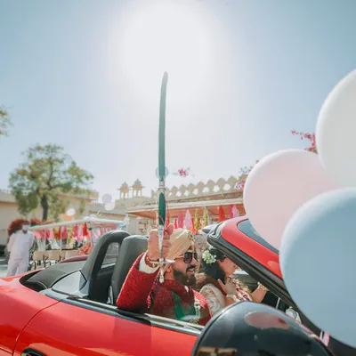 A grand entrance for the groom in a fiery red Porsche convertible, holding a traditional sword. This is how you make a statement and kick off the baraat with style and energy.