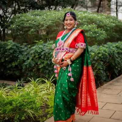 A full-length portrait of the mom-to-be at her outdoor Dohale Jevan, looking radiant in a traditional green and red Paithani saree.