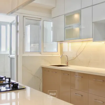 This kitchen showcases an elegant and bright design with high-gloss beige lower cabinets and white upper cabinets. The space feels open and airy, with a utility balcony accessible directly from the kitchen.