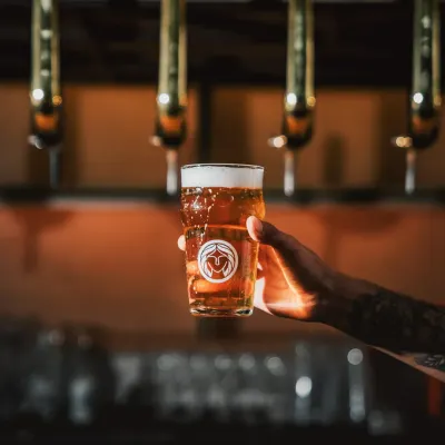 A freshly poured glass of one of our 16 craft beers, held up against the warm glow of the bar taps. Each brew is selected for its quality and character.