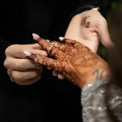 A close-up of the ring exchange, a pivotal moment in any engagement ceremony. I focus on details like the henna and the couple's initial tattoo.