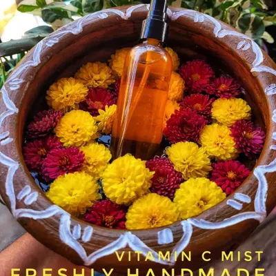 My handmade Vitamin C Mist, beautifully staged in a bowl of fresh flowers. This hydrating toner helps prevent premature aging, treats sun damage, and brightens your complexion with every spray.