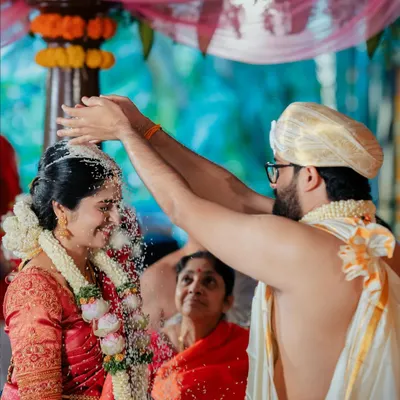 A sacred moment as the groom showers the bride with rice, a significant ritual in many South Indian weddings, captured with a focus on her joyful expression.